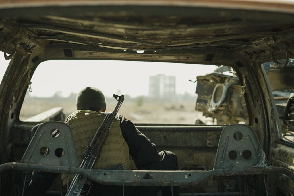 Armed resistance fighter crouched behind an abandoned vehicle for cover, gun at the ready.